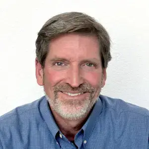 Steve MacDonald smiling in a blue shirt against a white background